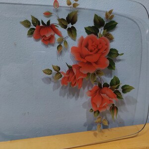 Pode incluir: Uma bandeja de servir de vidro transparente com um design floral com rosas vermelhas e folhas verdes.