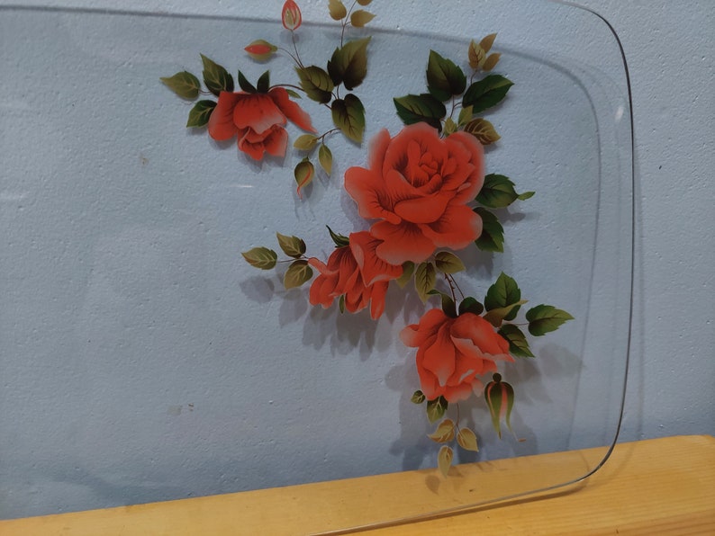 Pode incluir: Uma bandeja de servir de vidro transparente com um design floral com rosas vermelhas e folhas verdes.