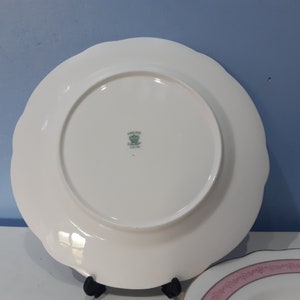 May include: White ceramic dinner plate with a scalloped edge and a green and white logo that reads "Landau Fine China England" with a crown above the text.