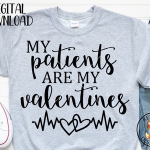 Pode incluir: Uma camisola cinzenta com o texto "Meus pacientes são meus valentin@s" em fonte cursiva preta. Dois corações entrelaçados com uma linha de batimento cardíaco estão abaixo do texto. O texto "Red Fox Designs US" está num círculo vermelho com uma ilustração de raposa vermelha.