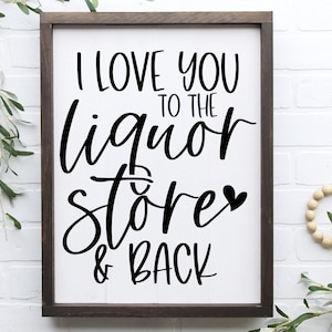 Pode incluir: Uma placa de madeira branca com texto preto que diz "I love you to the liquor store & back" com um pequeno símbolo de coração. A placa é emoldurada em uma moldura de madeira marrom escura.
