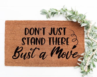 May include: A brown coir doormat with the text "Don't just stand there, Bust a Move" in black lettering.