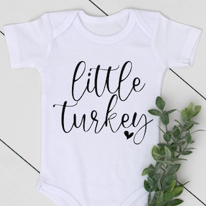 May include: White baby onesie with black text that reads "little turkey" and a small black heart.
