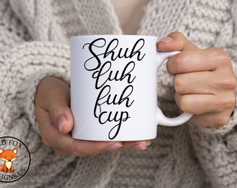 May include: White ceramic mug with black text that reads "Shuh  luh  fuh  cup".