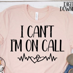 May include: A pink t-shirt with the text "I can't I'm on call" in black lettering. A heart beat graphic is below the text.