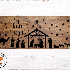 May include: A wooden sign with the text "Oh holy night" and a silhouette of the nativity scene with a star above the stable. The background is a brown wood grain.