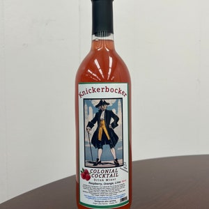 May include: A glass bottle of Knickerbocker Colonial Cocktail Drink Mixer, featuring a raspberry, orange, and lime flavor. The bottle has a vintage-style label with an illustration of a man in colonial attire.