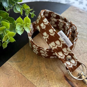 May include: A brown and white floral lanyard with a silver clasp. The lanyard features a repeating pattern of white tulip-like flowers on a brown background. The text "October Days" is printed on a small white tag.