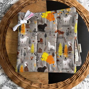 May include: Grey quilted pot holder with a forest animal print featuring bears, deer, and owls. The pot holder has a white ribbon and a metal grommet. The words "October Days" are printed on a small tag.