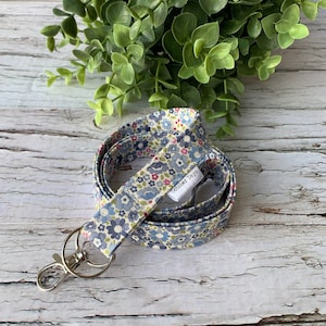 May include: A blue and white floral patterned lanyard with a silver swivel clip and a white tag that says "October Days".