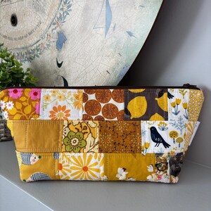 May include: A yellow, brown and white patchwork zippered pouch with a variety of patterns, including lemons, flowers and birds.