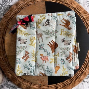 Peut inclure: Un dessous de plat matelassé bleu clair avec un motif d'animaux de la ferme : chèvres, moutons et vaches. Le dessous de plat a un nœud rouge et noir et un œillet métallique. Le dessous de plat mesure environ 20 cm de côté.