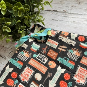 May include: Black fabric with a autumn-themed print featuring trucks, pumpkins, gourds, and signs that say "Farm Fresh", "Hay Rides 75p", and "Fresh Apple Cider".