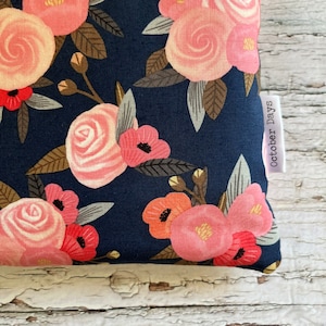 May include: A navy blue fabric pouch with a pink and white floral pattern. The pouch has a white label with the text "October Days" printed on it.