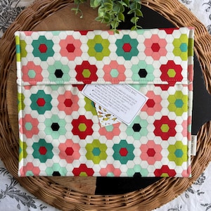 May include: A patterned microwave potato bag with a floral design. The bag displays a repeating pattern of red, green, and pink flowers on a white backdrop. A tag on the bag reads "Potato Bag" and provides instructions. Made from 100% cotton.