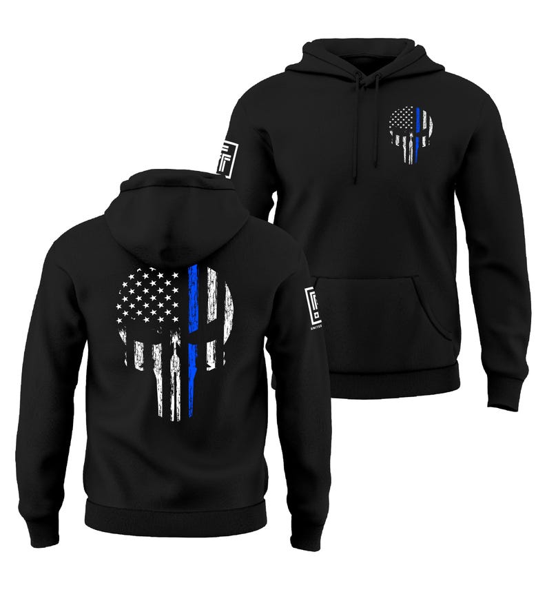 May include: Black hoodie featuring a skull design with the American flag and a blue line. The design is on the front and back of the hoodie. The hoodie has a hood and a front pocket.