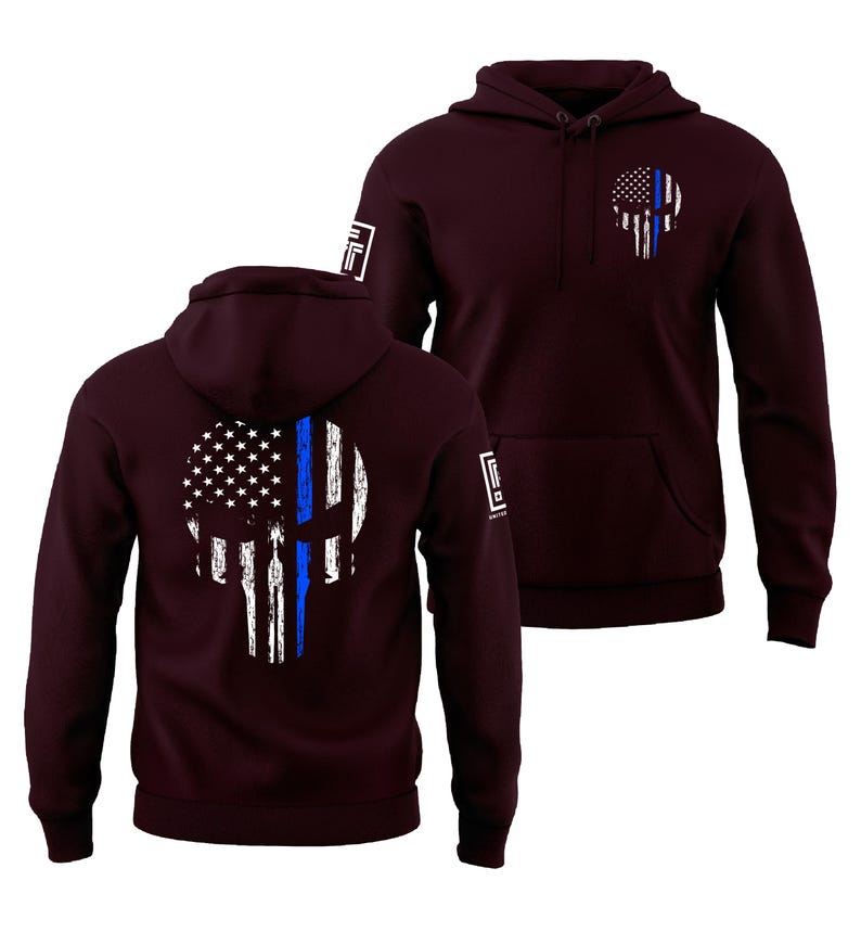 May include: Burgundy hoodie featuring a skull design with an American flag and a blue line. The design is on the front and back. The hoodie has a hood and a front pocket. The sleeves have a small white logo.