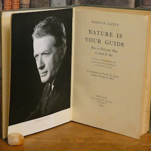 Op de afbeelding: Open boek met de titel "Nature Is Your Guide" van Harold Gatty. De kaft van het boek toont een zwart-wit portret van een man. Het boek is open en toont tekst en een portret.