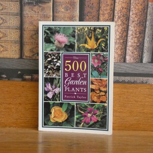 May include: A hardcover book titled The 500 Best Garden Plants by Patrick Taylor. The white cover features a central maroon rectangle with gold text and eight surrounding square photographs of various colorful flowers and foliage.
