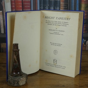 Op de afbeelding: Een vintage boek getiteld "Bright Tapestry" door Margaret M. Pearson, auteur van "London Adventure" etc. De boekomslag is wit met zwarte tekst en een klein zwart-wit zegel. Het boek ligt open op de titelpagina en ligt op een houten oppervlak.