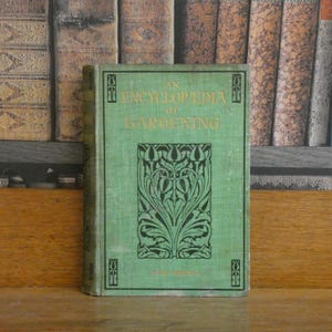 May include: A light green hardback book titled An Encyclopedia of Gardening with gold lettering on the front cover. The cover features a central black botanical illustration of stylised leaves and flowers, framed by a thin black border.