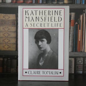 May include: A hardcover book titled Katherine Mansfield A Secret Life by Claire Tomalin. The white dust jacket features a black and white portrait of a person with short dark hair, framed by a thin red border with black text on the cover.