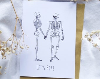May include: A greeting card with a black and white illustration of two skeletons holding hands. The text "LET'S BONE" is printed below the skeletons.