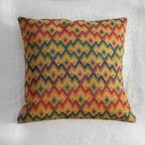 Op de afbeelding: Een decoratief kussen met een geometrisch patroon in tinten rood, oranje, geel, groen en blauw. Het patroon is een herhalend chevron-ontwerp.
