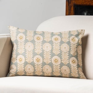 Könnte beinhalten: Ein hellblaues Kissen mit einem weißen und goldenen Blumenmuster. Das Kissen liegt auf einem weißen Sofa.