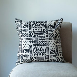 Peut inclure: Un coussin de décoration à motif géométrique noir et blanc sur un fauteuil beige clair.