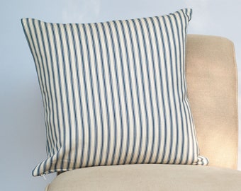 May include: A white and navy blue striped throw pillow on a beige chair. The pillow is made of a soft, woven fabric.