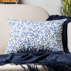 Könnte beinhalten: Ein rechteckiges Zierkissen mit einem blauen Korallenmuster auf weißem Hintergrund. Das Kissen liegt auf einem weißen Sofa mit einer marineblauen Decke.