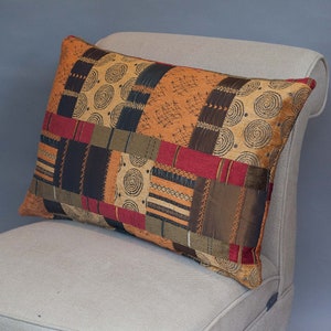 May include: A rectangular throw pillow with a patchwork design featuring various shades of brown, orange, red, and black. The pillow has a geometric pattern with swirls and lines.