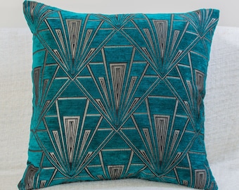 Puede incluir: Cojín azul turquesa con un patrón geométrico en plata y negro. El patrón recuerda al diseño Art Deco.