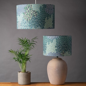 Peut inclure: Deux lampes avec des abat-jours à motifs verts et bleus. Le plus grand abat-jour est suspendu au plafond, tandis que le plus petit abat-jour est sur un pied de lampe de table en céramique beige.