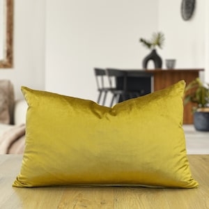 Peut inclure: Un grand coussin rectangulaire en velours jaune moutarde. Le coussin est posé à plat sur une surface en bois.