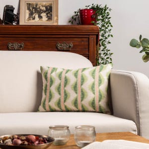 Könnte beinhalten: Ein rechteckiges Zierkissen mit einem grünen und weißen geometrischen Muster und roten vertikalen Streifen. Das Kissen liegt auf einem cremefarbenen Sofa. Das Design des Kissens verleiht dem neutral getönten Sofa einen Hauch von Farbe und Muster.