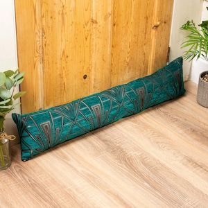 May include: A teal blue doorstop with a black and gold geometric pattern. The doorstop is made of fabric and is designed to prevent doors from slamming.