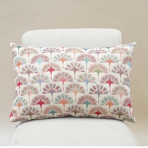 May include: A rectangular cushion with a white background and a colourful geometric pattern of stylised sunbursts in shades of red, orange, yellow, green, blue, and purple.