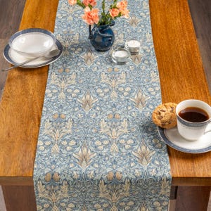 May include: A blue floral patterned table runner with a matching bowl, saucer, and cup. The table is set with a vase of flowers, candles, and a cookie. The runner is approximately 183 cm long.