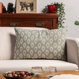 Op de afbeelding: Een rechthoekig decoratief kussen met een groen paisley patroon ligt op een witte bank. Het kussen heeft een herhalend druppelmotief in groen, wit en grijs. Het kussen voegt een vleugje elegantie toe aan de woonkamer.