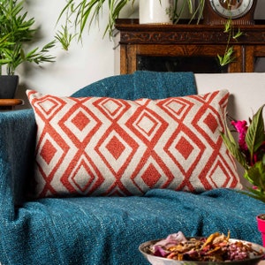 May include: A red and white geometric patterned cushion on a teal blue sofa. The cushion is rectangular and has a diamond pattern.
