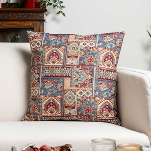 Peut inclure: Coussin carré décoratif avec un motif patchwork. Le coussin présente un motif de formes florales et géométriques bleues, rouges et beiges. Le coussin est placé sur un canapé blanc, ajoutant une touche de couleur et de motif à l'espace.