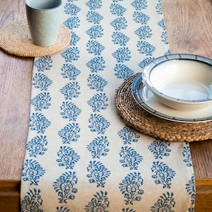 Könnte beinhalten: Ein weißer Tischläufer aus Leinen mit einem blauen Blumenmuster. Der Läufer ist mit blauen Blumenmotiven verziert und perfekt, um jeder Tischdekoration einen Hauch von Eleganz zu verleihen.