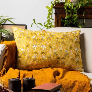 Può includere: Un cuscino giallo con un motivo floreale con piccoli uccelli e fiori. Il cuscino è su un divano con una coperta gialla senape.