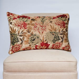 Può includere: Cuscino rettangolare con motivo floreale con fiori rossi, verdi e marroni su sfondo beige. Il cuscino è appoggiato su una sedia beige.