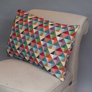 Puede incluir: Una almohada de tiro con un patrón geométrico colorido con una mezcla de tonos rojos, azules, verdes y amarillos. La almohada está sentada en una silla beige.