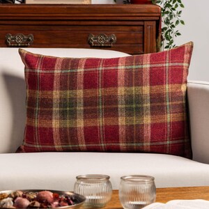 Könnte beinhalten: Ein rechteckiges Zierkissen mit einem rot, grün und goldfarbenen Karomuster. Das Kissen liegt auf einem weißen Sofa. Das Design zeigt ein klassisches Tartanmuster und verleiht jedem Wohnraum einen Hauch von Wärme und Stil. Misst ca. 40 cm x 60 cm.