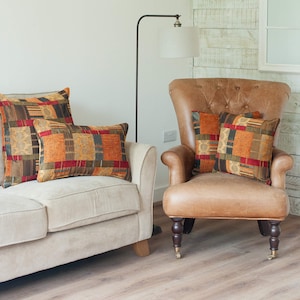 May include: Two sofas with patterned throw pillows in shades of orange, red, and brown. The sofas are positioned in a living room setting with a floor lamp and a wooden floor.