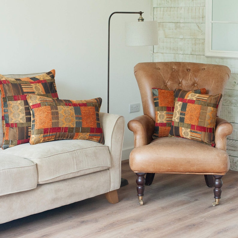 May include: Two sofas with patterned throw pillows in shades of orange, red, and brown. The sofas are positioned in a living room setting with a floor lamp and a wooden floor.